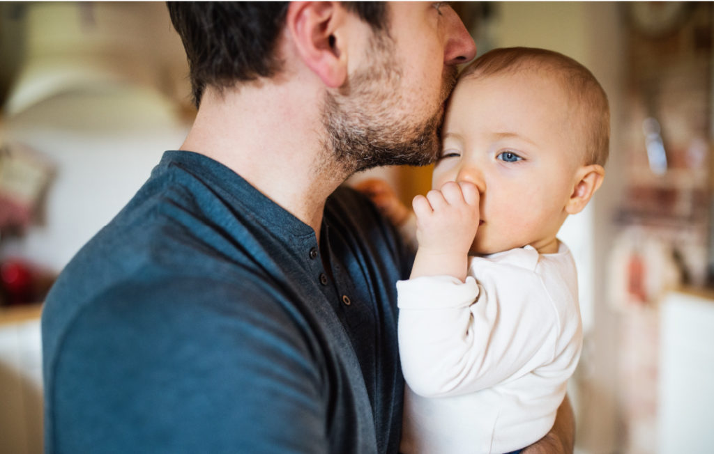 Papa tient dans ses bras son bébé qui se sent rassuré. Cette photo illustre l'article sur le parent préféré