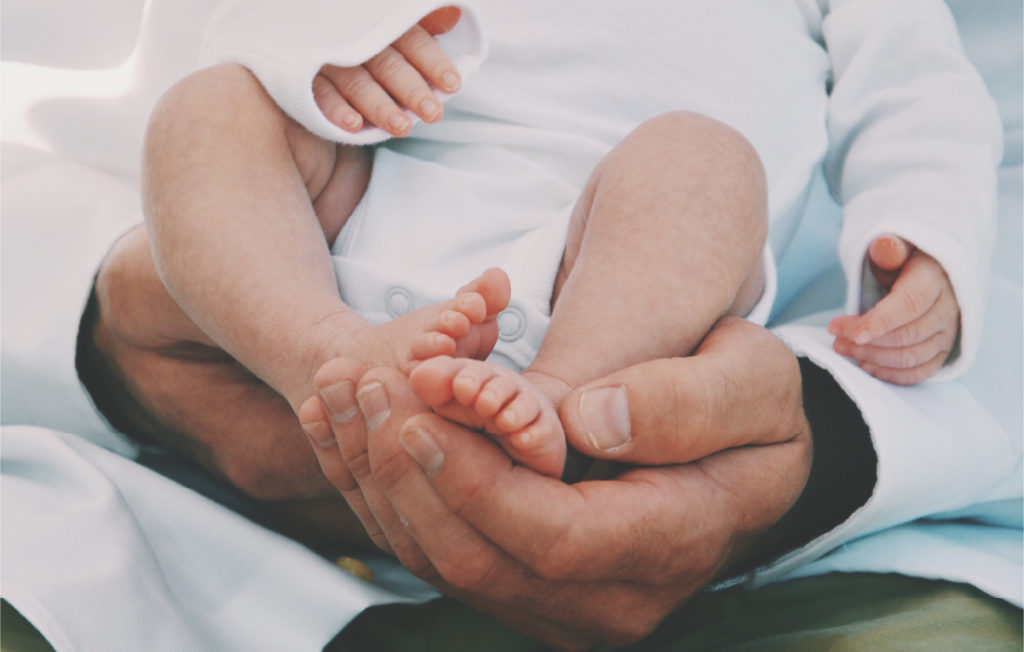 Un papa qui tient dans ses bras son bébé. Cette image illustrer le rôle du père.